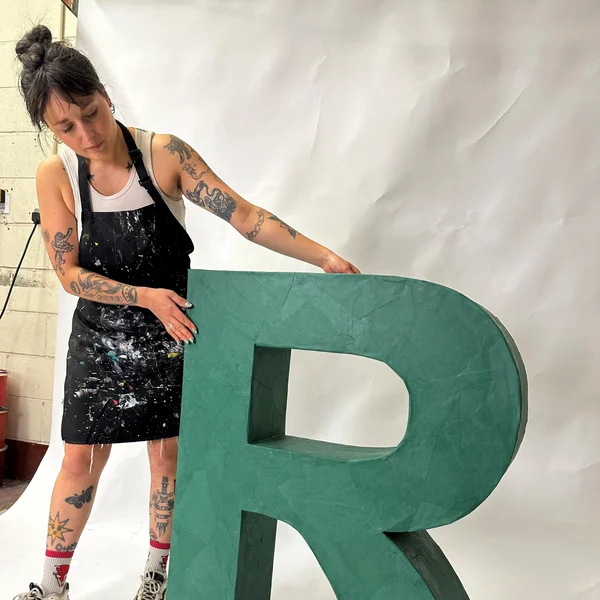 Workshop team member finishing a large green papier-mâché cardboard letter