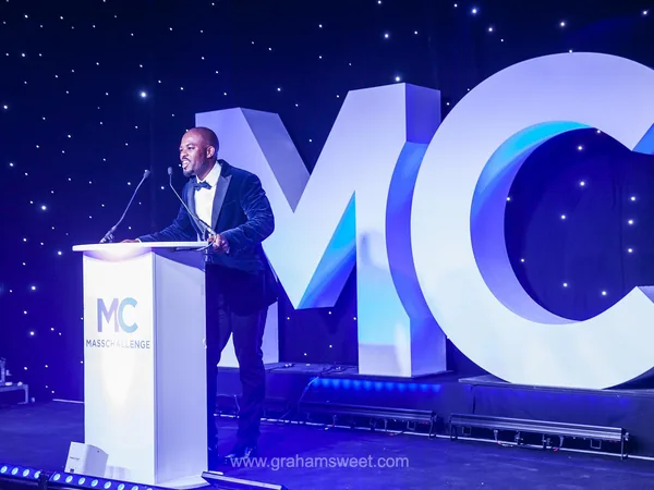 Speaker on stage beside oversized illuminated MC event letters
