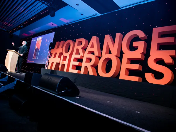 Large orange hashtag Orange Heroes letters on an event stage