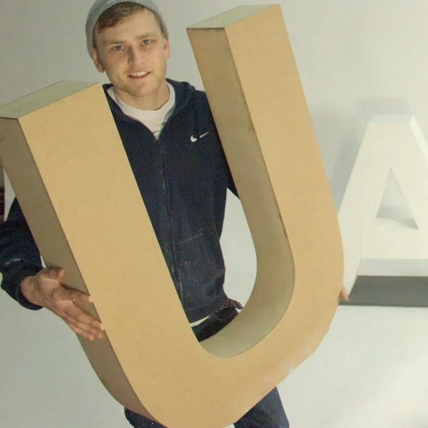 Workshop team member holding a large wooden U beside an A letter