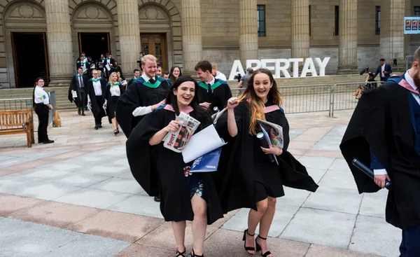 Graduates celebrating beside large Abertay University letters