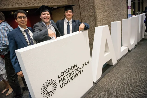 Graduates standing behind large London Metropolitan University letters
