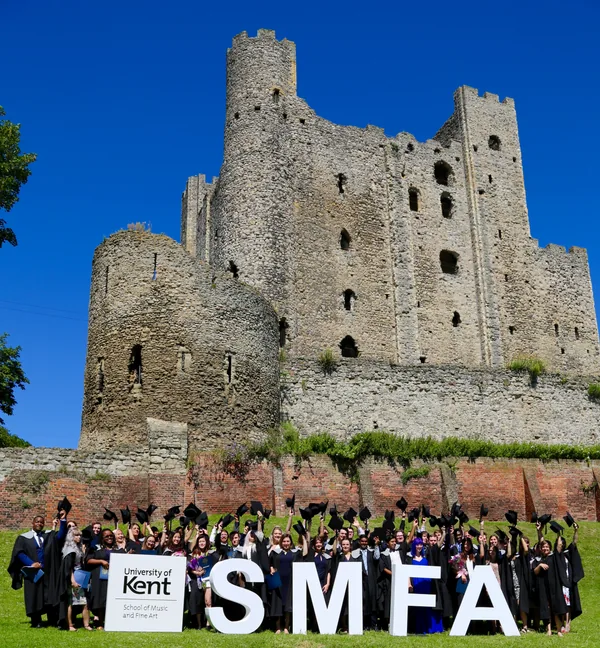 University of Kent graduates standing behind large SMFA letters