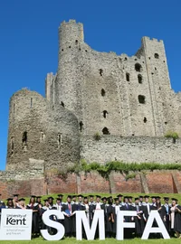 Graduates standing behind large SMFA letters at the University of Kent