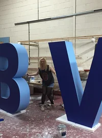 Workshop team member standing between oversized blue B and V letters