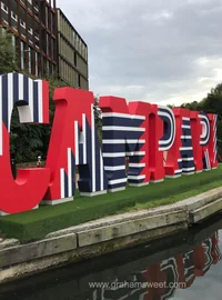 Large red white and blue striped display letters installed outdoors beside a canal