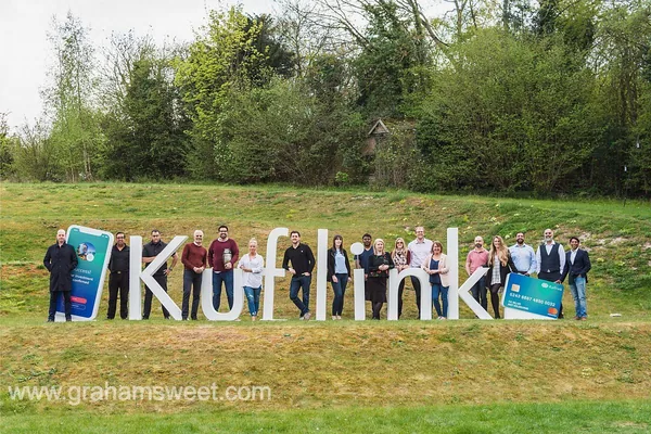 Team standing beside large white Kuflink letters and oversized product props
