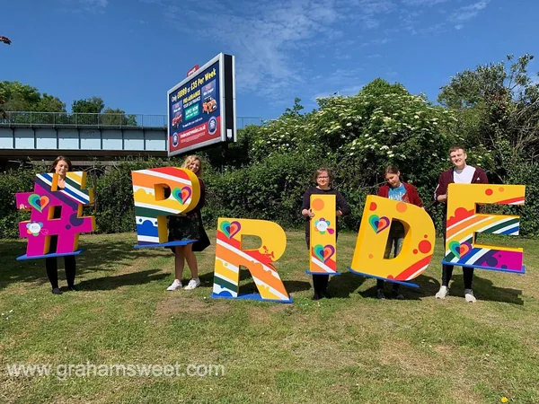 People holding colourful freestanding letters spelling Pride