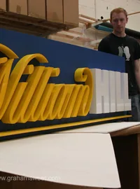 Gold Harrods script logo mounted on a dark display panel