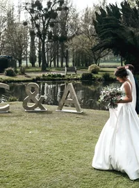 Bride walking near silver glitter initials beside a lake