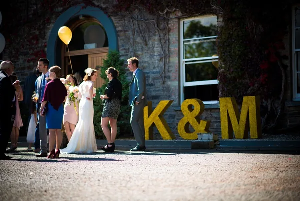 Wedding guests gathered beside large gold glitter initials at a venue