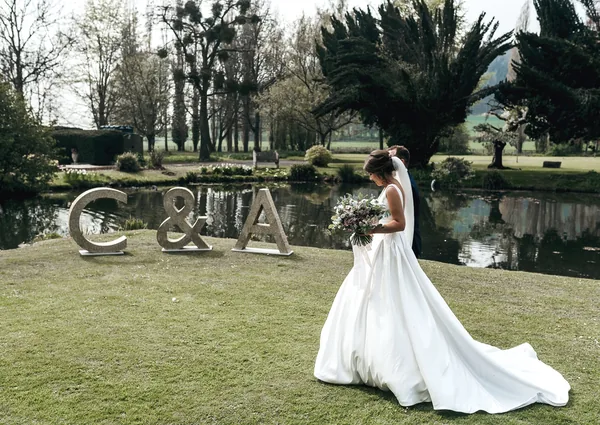 Bride walking beside silver glitter wedding initials at a lakeside venue