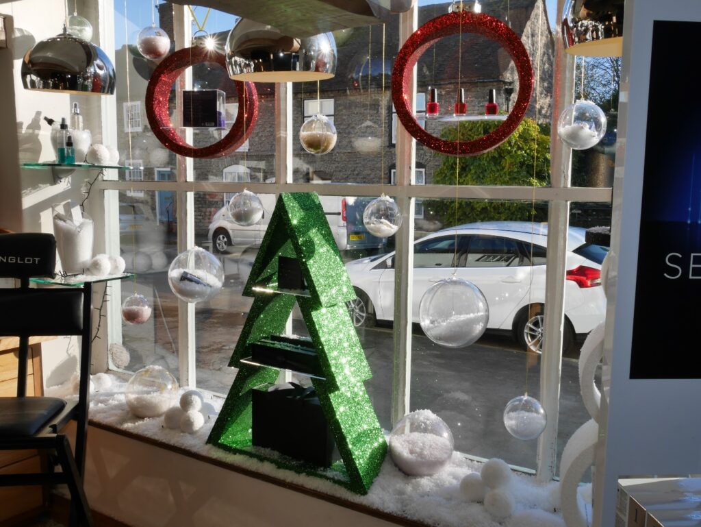 Christmas salon window with red bauble shelves, silver hanging baubles and a green tree display