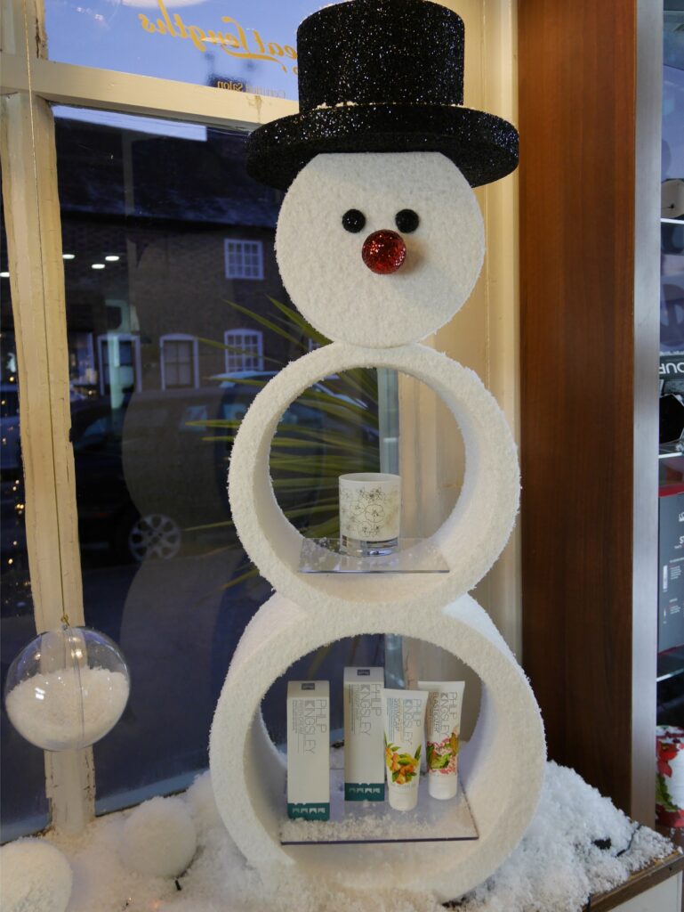 Snowman-shaped Christmas product display shelf in a salon window