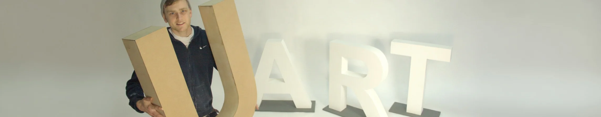 Craftsman holding a large wooden letter U beside freestanding MDF letters