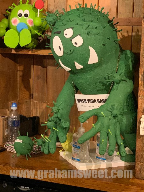 Large green model flu bug, with 3 eyes, and a sign saying wash your hands - sat behind the bar at a pub.