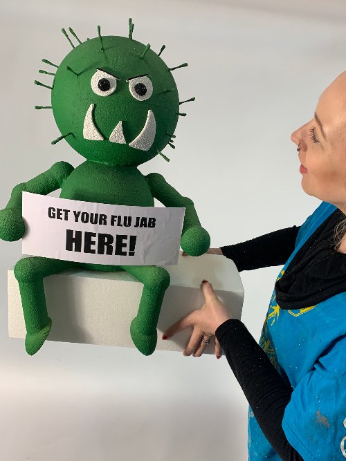 Large green model flu bug, with 2 eyes, and a sign saying Get your flu jab here.