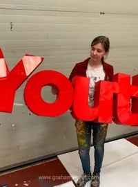 Woman holding large red Youth display letters